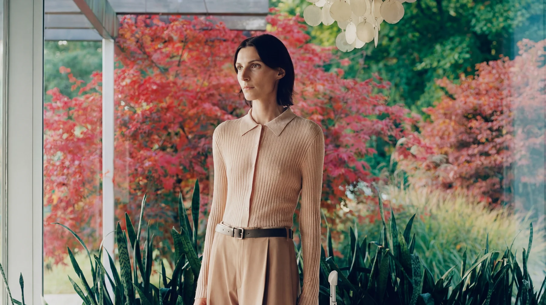 Woman in neutral fashion beside a vivid garden window