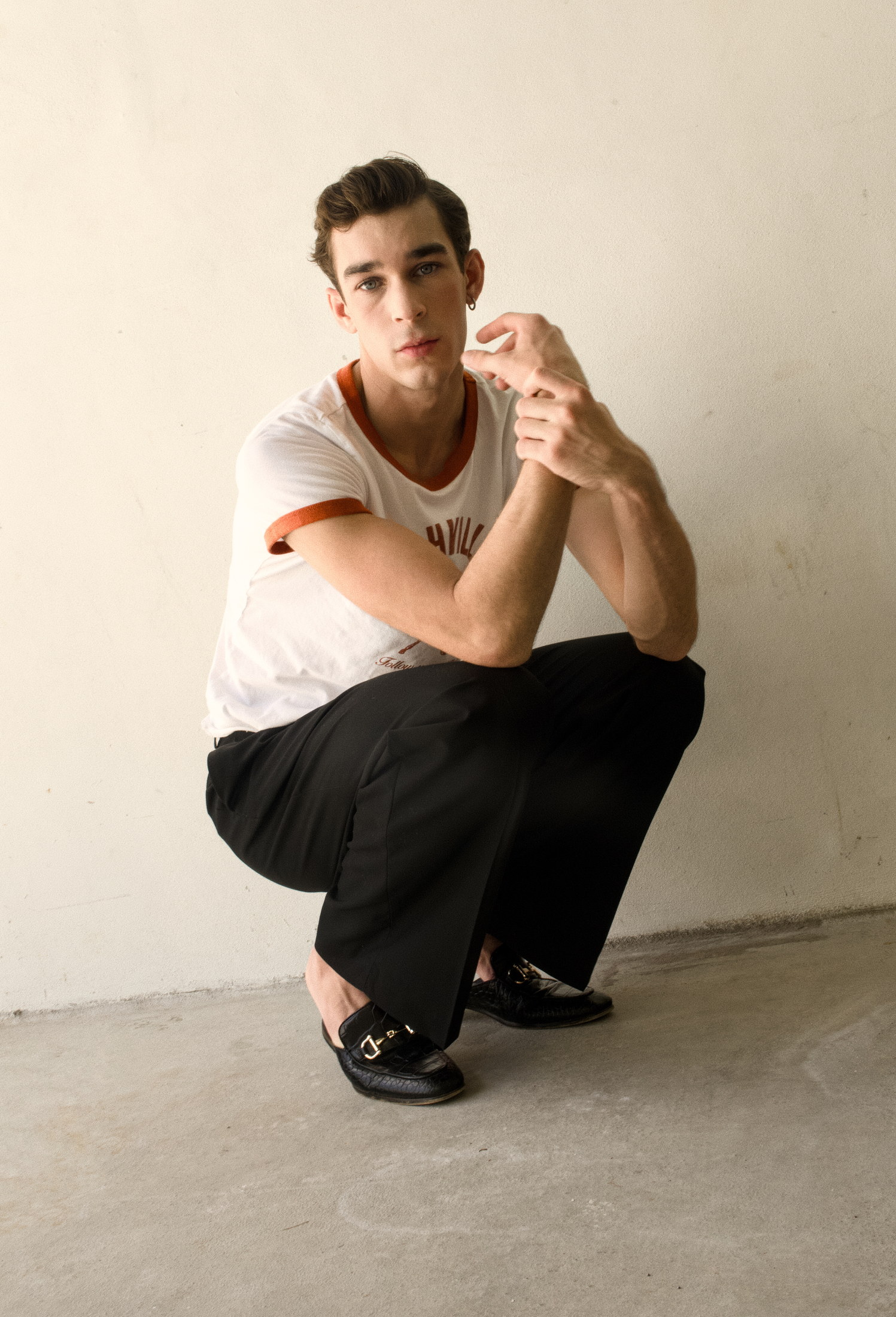 Editorial menswear portrait crouched against a minimal wall
