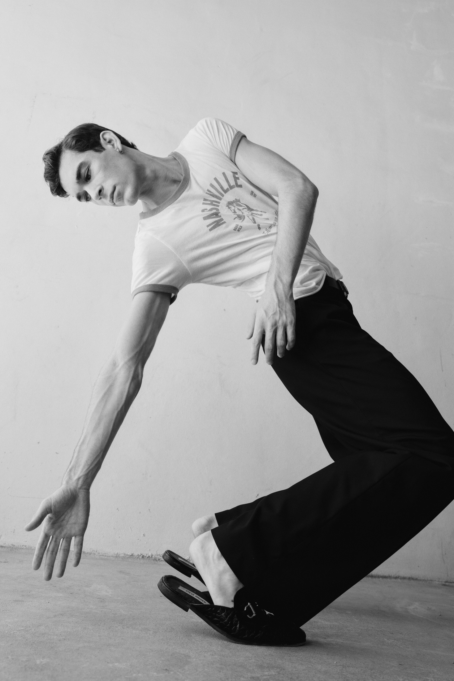 Black-and-white menswear movement portrait with a low sweeping gesture