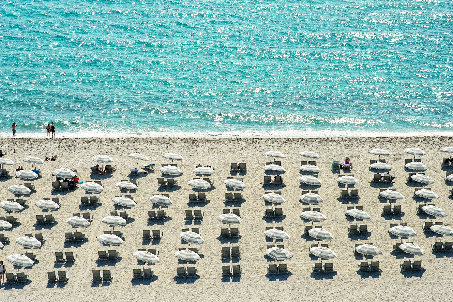 Aerial view of turquoise water and repeating beach umbrellas